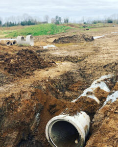 Concrete pipe sections laid in an open drainage trench on a cleared site