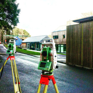 Two total stations set up on tripods outside a timber clad school building