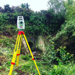 Total station set up beside a concrete culvert entrance in heavy vegetation