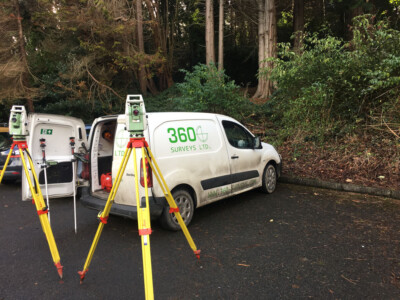 Two total stations on tripods beside the 360 Surveys Ltd van in woodland