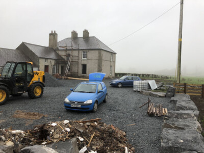Farmhouse under renovation with a telehandler and materials in the yard