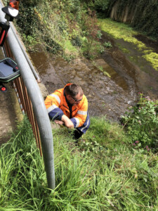 Surveyor in high visibility clothing taking a measurement at a stream