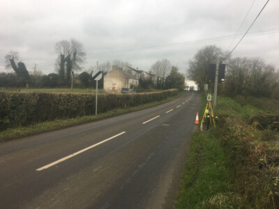 Survey tripod and traffic cone set up on the verge of a rural road