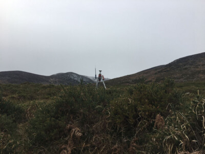 Total station on a tripod on open moorland below a mountain ridge
