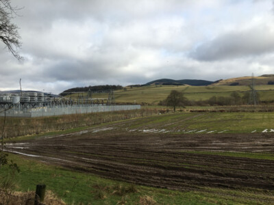Industrial tank farm and pipework seen across a ploughed field