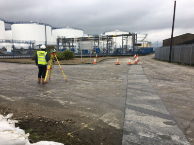 Surveyor in high visibility clothing with a tripod at a fuel tank depot