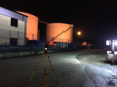 Survey tripod at night in front of illuminated bulk storage tanks