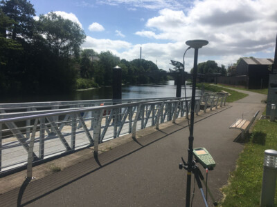 GNSS receiver on a pole set up on a riverside walkway with railings