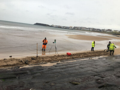 Surveyors in high visibility clothing working on a beach beside a slipway