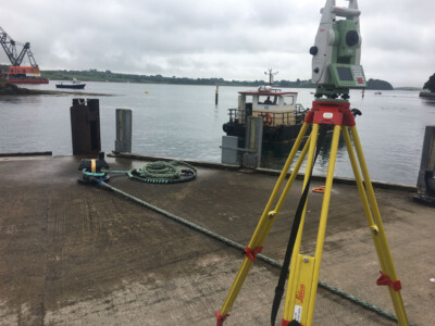 Total station on a quayside with a crane barge moored on the water behind