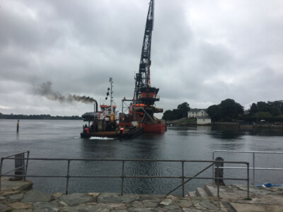 Dredger with a crane working on the water, viewed from the quay railings