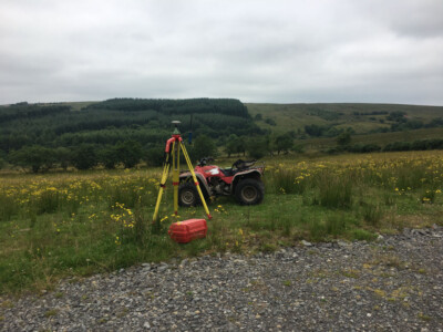 Total station and quad bike on rough upland ground with forestry behind