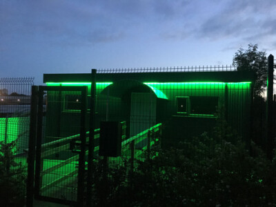 Security fencing lit green at night in front of an industrial building
