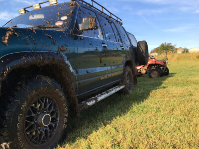 Mud splattered four wheel drive towing a quad bike trailer across a field